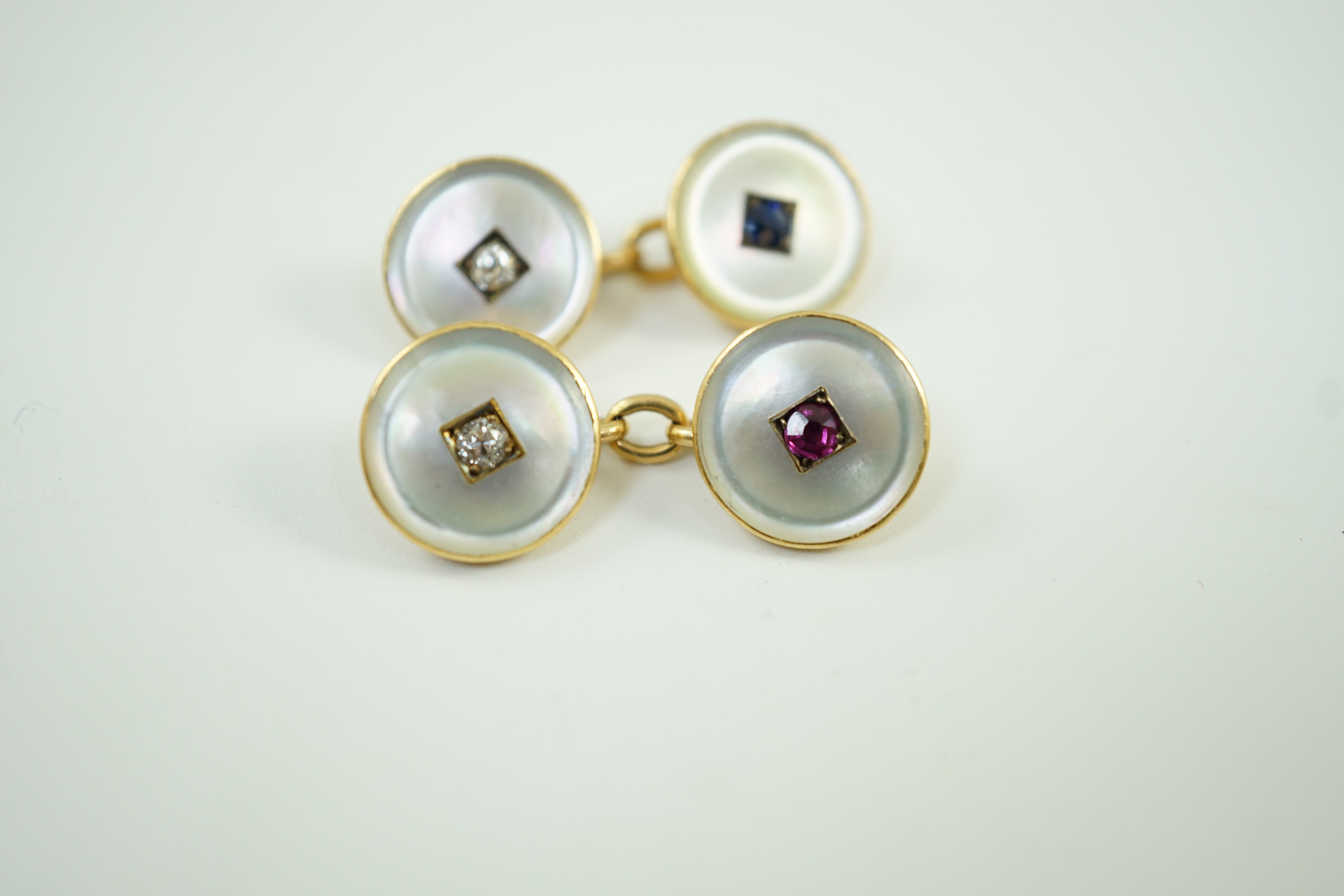 A pair of early to mid 20th century yellow metal mounted mother of pearl and gem set cufflinks, one set with a ruby and diamond, the other with a sapphire and diamond, link diameter 12mm, gross weight 8 grams.